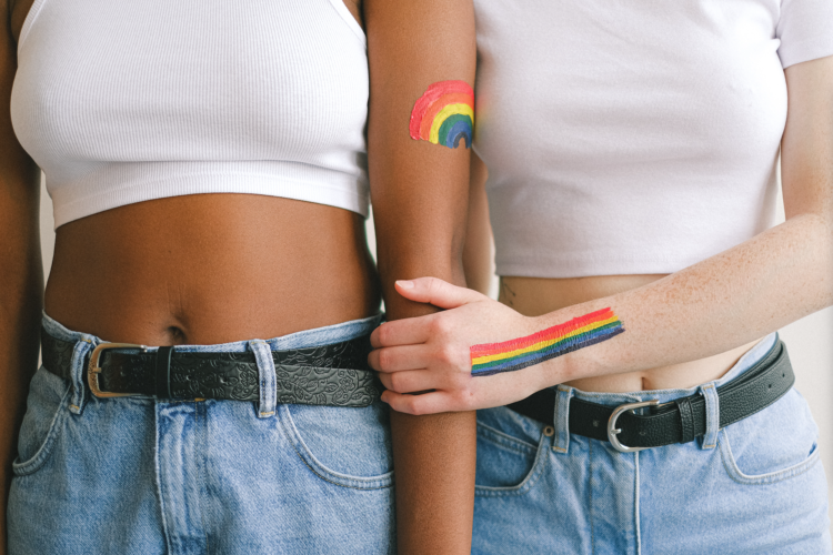 Dos mujeres tomadas de la mano con banderas arcoiris pintadas en la piel