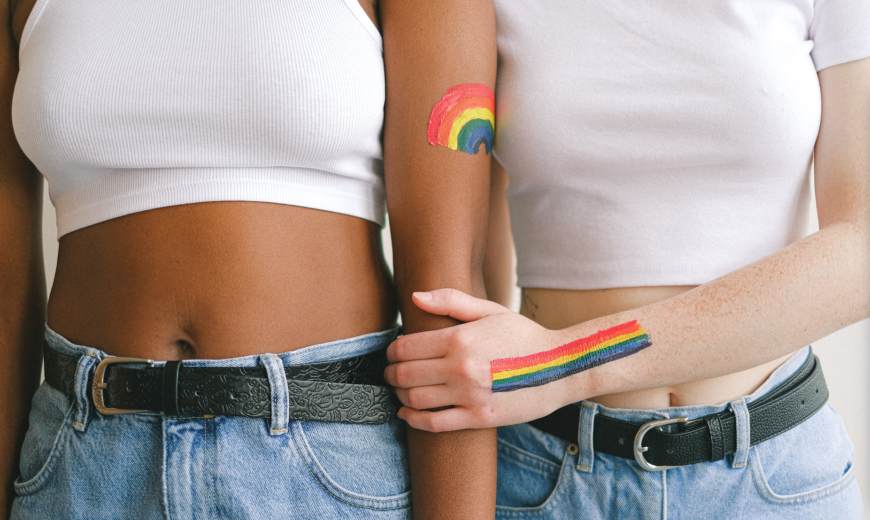 Dos mujeres tomadas de la mano con banderas arcoiris pintadas en la piel